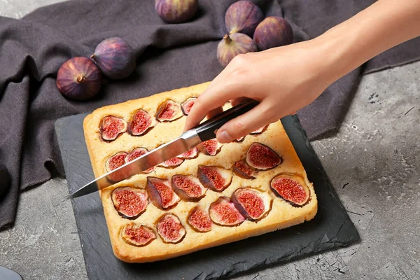 Woman cutting delicious fig pie on grunge background