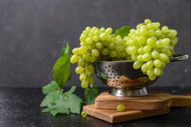 Colander with ripe green grapes on dark background