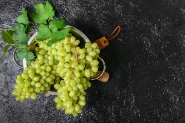 Colander with ripe green grapes on dark background