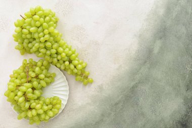 Plate with ripe green grapes on light background