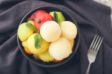 Bowl with sweet fruit balls on fabric background