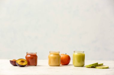 Jars with different baby food and ingredients on light background