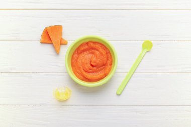 Bowl with pumpkin baby puree, spoon and pacifier on white wooden background