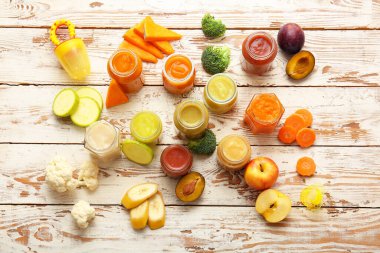 Jars with different baby food and ingredients on light wooden background