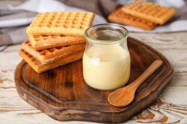 Kavanoz, tatlı yoğunlaştırılmış süt ve ahşap arka planda waffle.