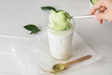 Kadın hafif ahşap arka planda lezzetli dalgona matcha latte hazırlıyor.