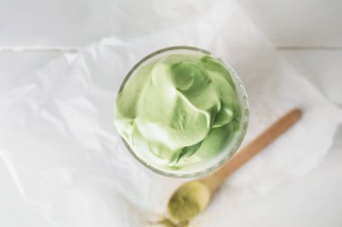 Bir bardak lezzetli dalgona matcha latte ve hafif ahşap arka planda kaşık, yakın plan.