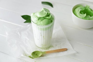 Bir bardak lezzetli dalgona matcha latte ve hafif ahşap arka planda kaşık