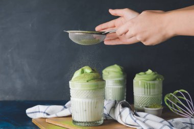 Kadın koyu arkaplanda lezzetli dalgona matcha latte hazırlıyor.