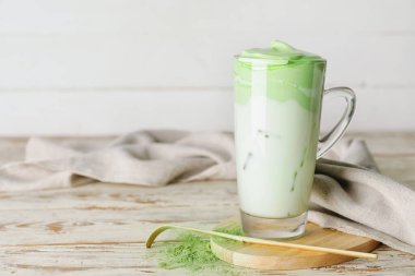 Hafif ahşap arka planda bir fincan lezzetli dalgona matcha latte, toz ve chashaku.