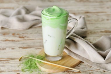 Hafif ahşap arka planda bir fincan lezzetli dalgona matcha latte, toz ve chashaku.