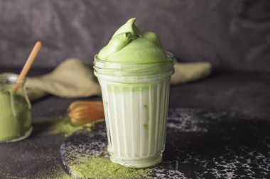 Bir bardak lezzetli dalgona matcha latte, koyu arkaplanda, yakın plan.