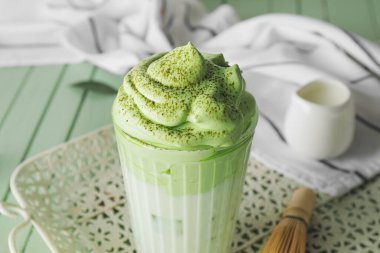 Bir bardak lezzetli dalgona matcha latte renkli ahşap arka plan, yakın plan