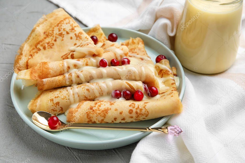 Plate with thin pancakes, cranberries and condensed milk on grey background