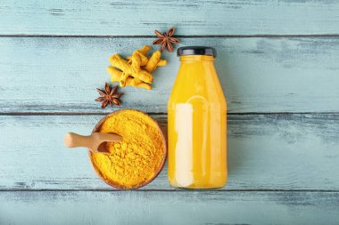 Bir şişe sağlıklı zerdeçal içeceği ve renkli ahşap arka planda pudra ile kase.