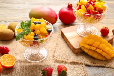 Tahta arka planda tropikal meyve salatası olan cam kaseler.
