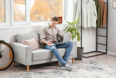 Evde dizüstü bilgisayar kullanan yakışıklı bir genç.