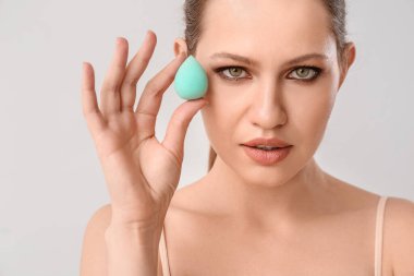 Açık arkaplanda makyaj süngeri olan güzel bir genç kadın.