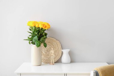 Odadaki ışık duvarının yanındaki masada güzel sarı güller olan vazo.