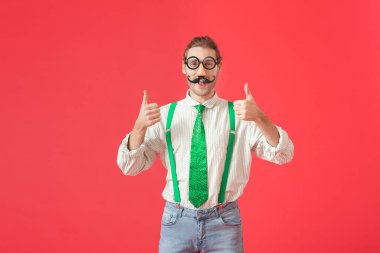 Renkli arka planda baş parmak hareketi gösteren komik kılık değiştirmiş genç bir adam. 1 Nisan şakası