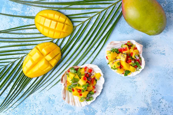 Sea shells with fresh mango salsa on color background