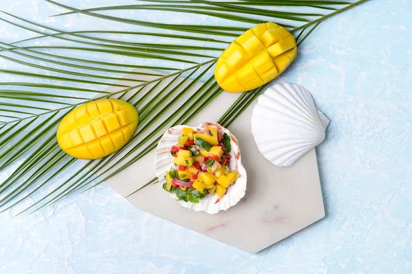 Sea shell with fresh mango salsa on color background