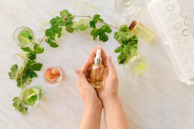 Üzüm tohumu yağı şişesi ve beyaz arka planda laboratuvar mataraları olan kadın elleri.