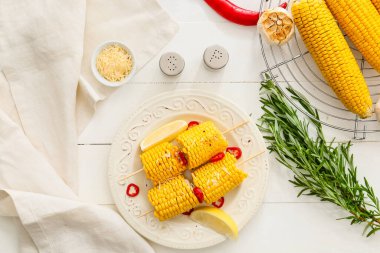 Hafif ahşap zemin üzerinde lezzetli pişmiş mısır koçanları olan bir tabak.
