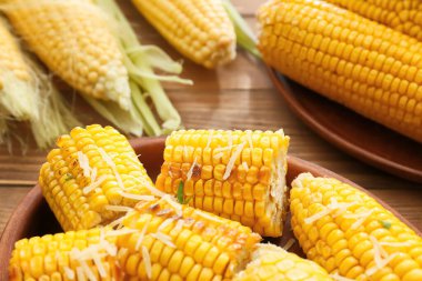 Ahşap zemin üzerinde lezzetli fırınlanmış mısır koçanları olan yemek tabağı.