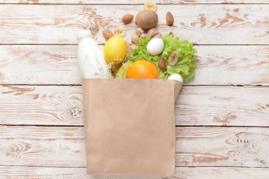 Açık ahşap zemin üzerinde farklı ürünler bulunan kağıt torba.