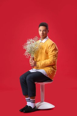 Çiçekli yakışıklı bir gencin portresi renk arka planına karşı taburede oturuyor.