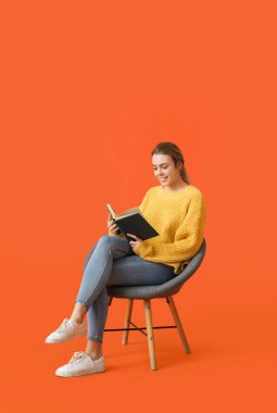 Güzel genç bir kadın, arka planda koltukta otururken kitap okuyor.