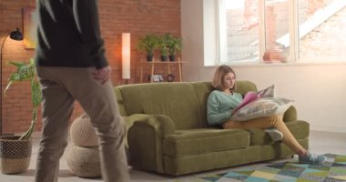 Genç kız dergi okuyor ve kanepede otururken babasını dinlemeyi reddediyor.