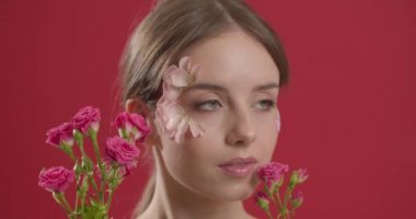 Yüzünde taç yaprakları ve renk arka planında bir buket çiçekle güzel bir genç kadın.