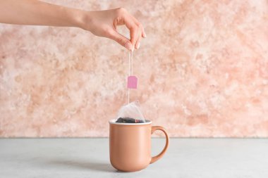 Kadın çay poşetini renkli arka planda fincana daldırıyor