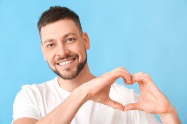Man making heart with his hands on color background clipart