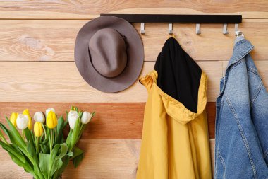 Elbiseli askı ve salonun ahşap duvarının yanında bahar çiçekleri.