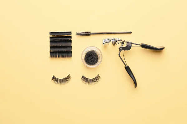 Curler, brush and false eyelashes on color background