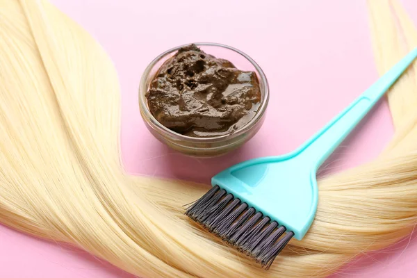 Bowl with henna, hair and brush on color background, closeup