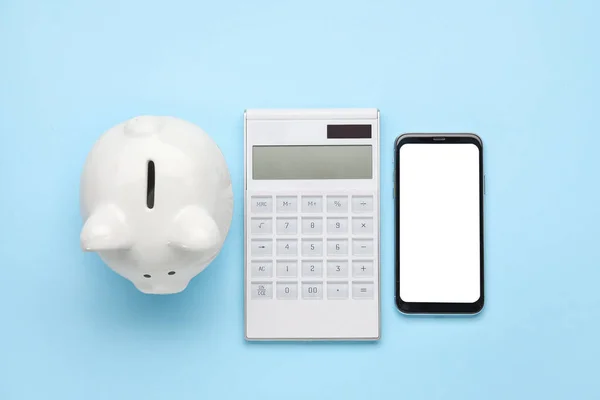 Calculator with mobile phone and piggy bank on color background