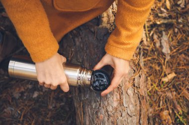 Termoslu genç bir kadın ormanda sıcak çay içiyor, yakın plan.