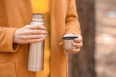 Termoslu genç bir kadın ormanda sıcak çay içiyor, yakın plan.