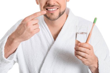 Ağrıyan dişleri, bir bardak su ve beyaz arka planda diş fırçası olan bir adam.