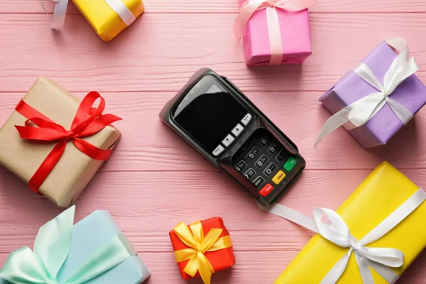 Payment terminal with gifts on color wooden background