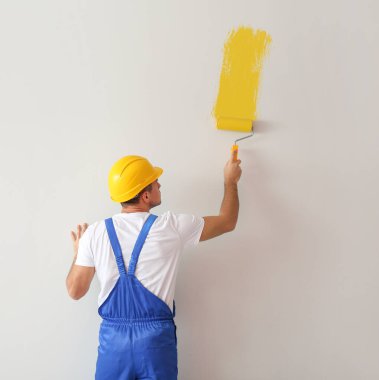 Genç erkek dekoratör ışık duvarı boyuyor.