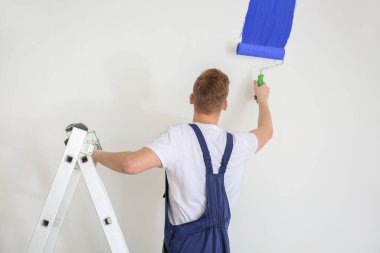 Işık duvarı boyamak için silindir kullanan erkek ressam