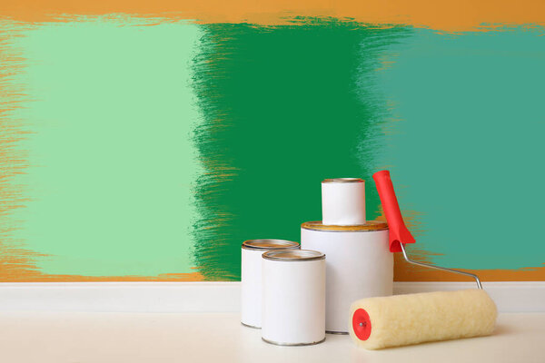 Cans of paints and roller on floor near colorful wall