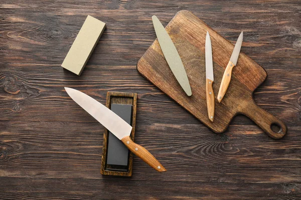 Board with set of knives and sharpening stone on wooden background