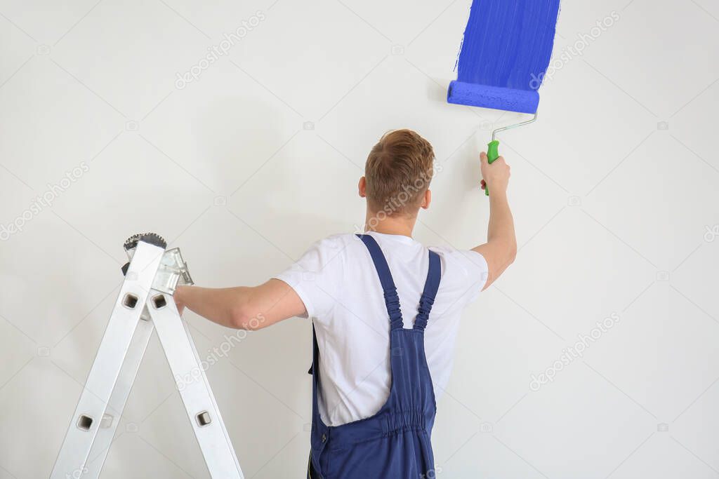 Male painter using roller for painting light wall