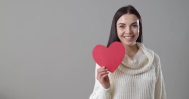 Gri arka planda kırmızı kağıt kalpli güzel bir kadın öpüşüyor.